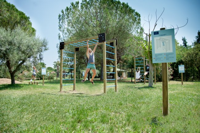 Una persona si esercita su una struttura da ginnastica all'aperto, circondata da alberi.