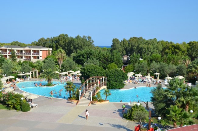 Una piscina con un ponte nel mezzo, circondata da alberi e lettini.