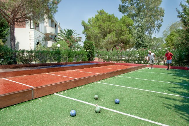 Campo da bocce all'aperto con due persone che giocano, circondato da alberi.