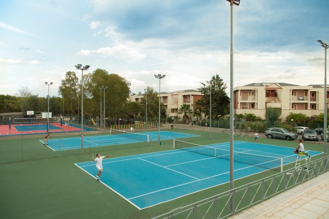 Campi da tennis all'aperto con persone che giocano, circondati da edifici e alberi.