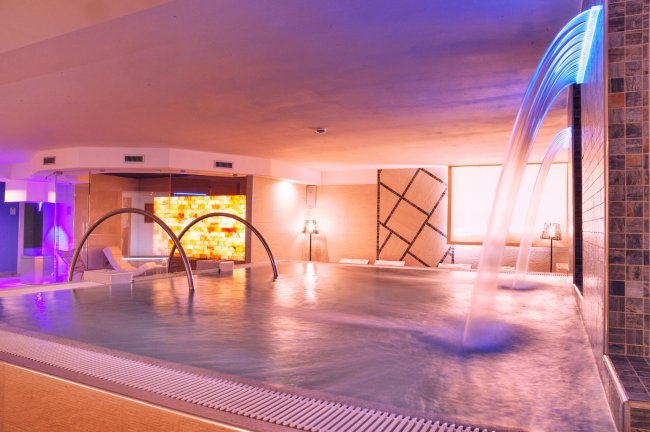 Spa con piscina interna, archi metallici e cascate d'acqua.