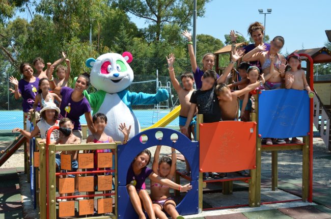 Gruppo di bambini e adulti in un parco giochi con un costume da panda sorridente.