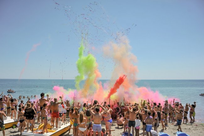 Una folla sulla spiaggia lancia polveri colorate in aria.