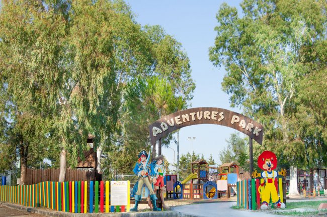 Ingresso di un parco avventura con recinzione colorata e figure di cartone animato.