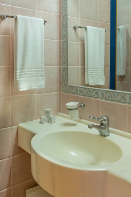 Un bagno con lavabo bianco, asciugamani appesi e specchio grande.
