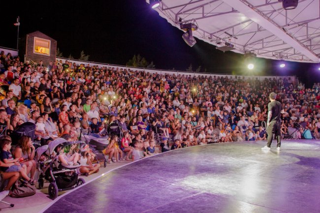Un pubblico numeroso in un anfiteatro all'aperto, illuminato di notte.