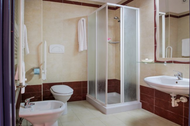 Bagno con doccia angolare in vetro, lavabo e bidet, rifiniture in marrone.