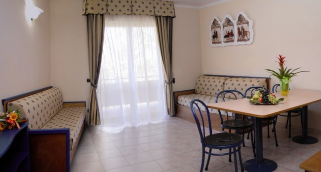 Soggiorno con due divani, tavolo con sedie, tende a righe e decorazione sulla parete.
