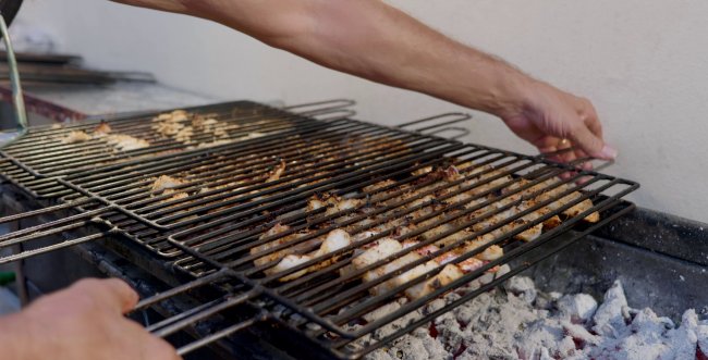 Mani che sistemano una griglia sopra il barbecue.