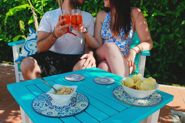 Coppia brinda con cocktail ad un tavolino all'aperto.