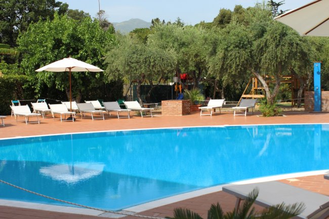 Piscina all'aperto con lettini e ombrellone bianco.