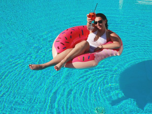 Persona in piscina su ciambella gonfiabile con drink arancione.