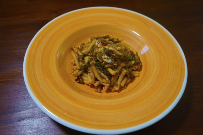 Piatto di pasta condita in un piatto arancione su tavolo di legno.