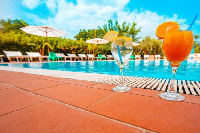 Due cocktail a bordo piscina con lettini e ombrelloni sullo sfondo.