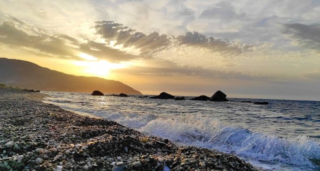 Spiaggia con onde al tramonto e montagne sullo sfondo.
