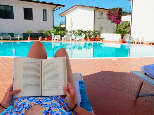 Persona legge a bordo piscina con case sullo sfondo.