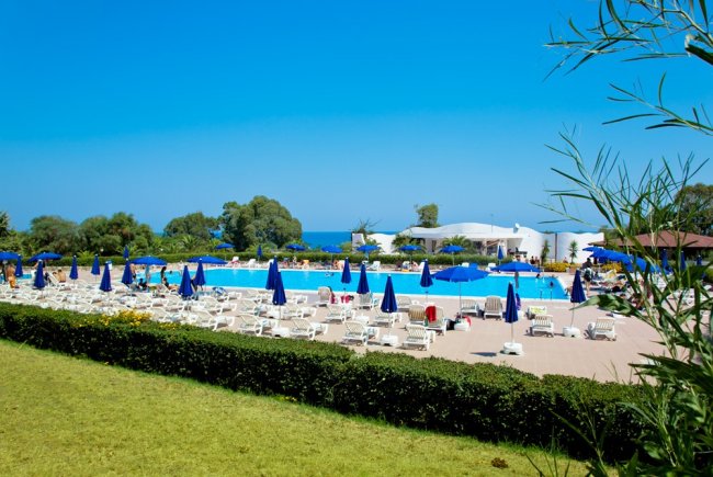 Piscina con ombrelloni blu, veduta di alberi e mare sullo sfondo.