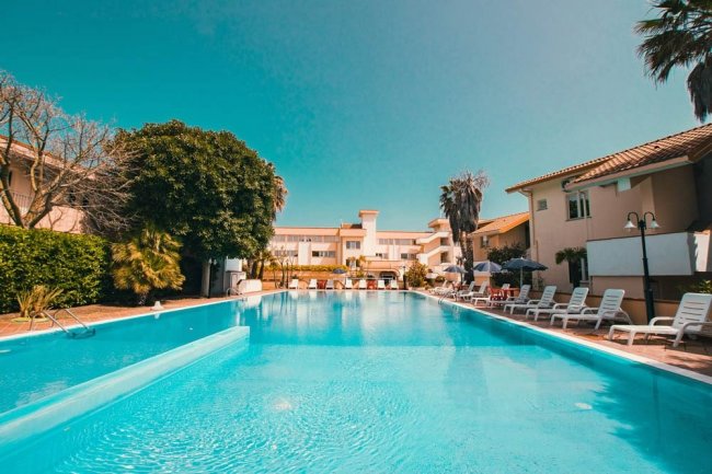 Piscina all'aperto con lettini e ombrelloni, circondata da edifici.