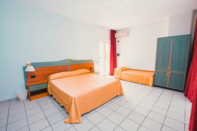 Camera con letto matrimoniale arancione, letto singolo, armadio verde, tende rosse.