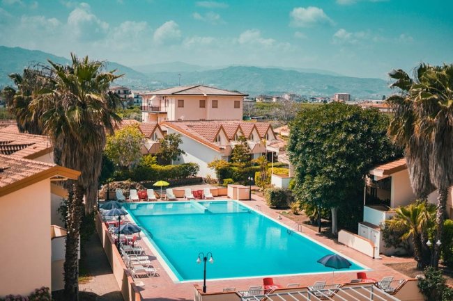 Piscina all'aperto circondata da palme e lettini, vista panoramica.
