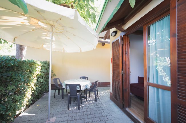 Terrazza con tavolo circolare, sedie nere e grande ombrellone bianco accanto a una porta-finestra.