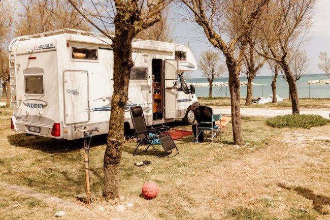Camper parcheggiato vicino ad alberi e mare.