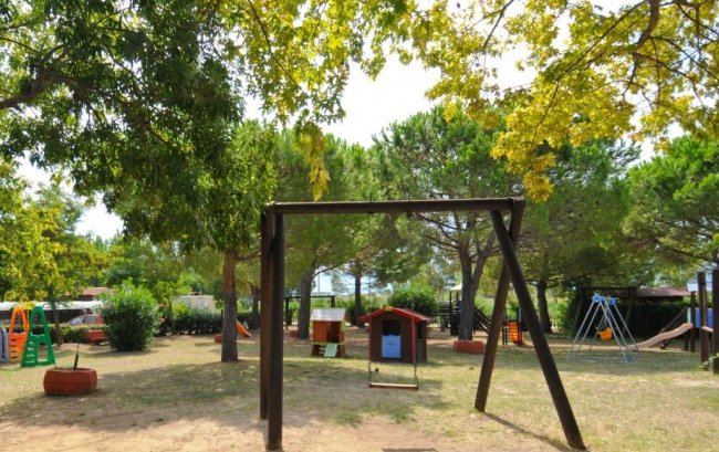 Parco giochi all'aperto con alberi, altalene e giochi per bambini.