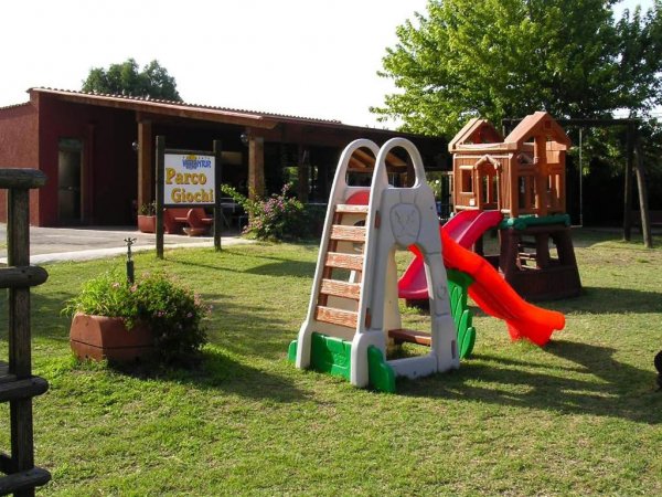 Un parco giochi con strutture per bambini su erba, tra cui uno scivolo rosso.