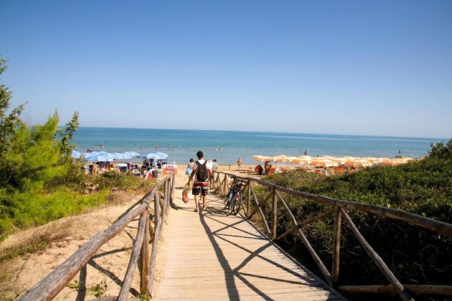Un sentiero di legno conduce a una spiaggia con ombrelloni, vista sul mare.