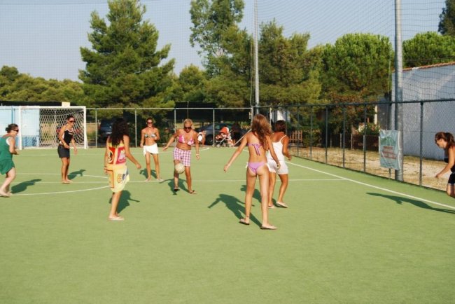 Gruppo di giovani che giocano a calcio su un campo all'aperto, con alberi sullo sfondo.