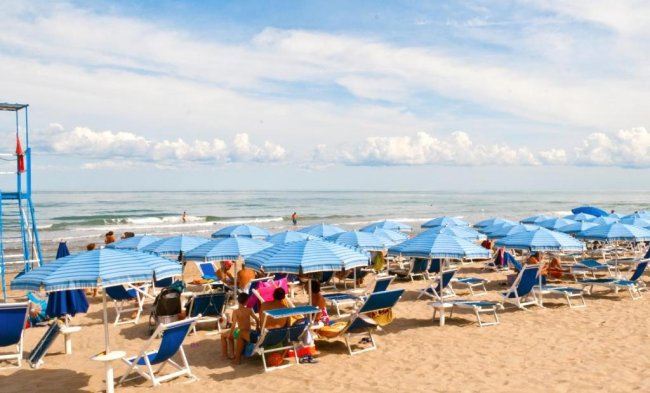 Spiaggia affollata con ombrelloni blu e lettini, vicino al mare calmo sotto un cielo nuvoloso.