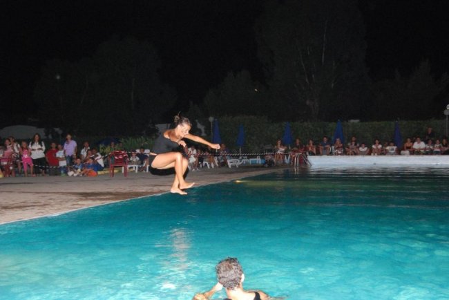 Una persona salta in aria sopra una piscina con spettatori seduti intorno di notte.