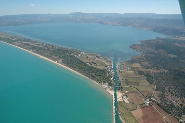 Vista aerea di un canale che collega un lago al mare con terreni e colline circostanti.