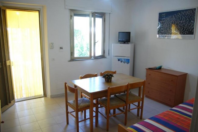 Sala con tavolo e sedie, divano colorato, TV su frigorifero e una finestra.