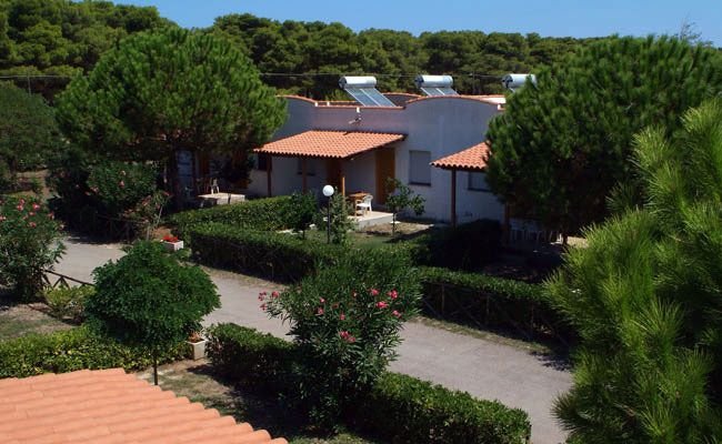 Capanne con tetti in tegole tra gli alberi, con vialetti e giardini curati.