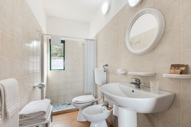 Bagno con doccia, lavabo e sanitari bianchi su piastrelle beige.
