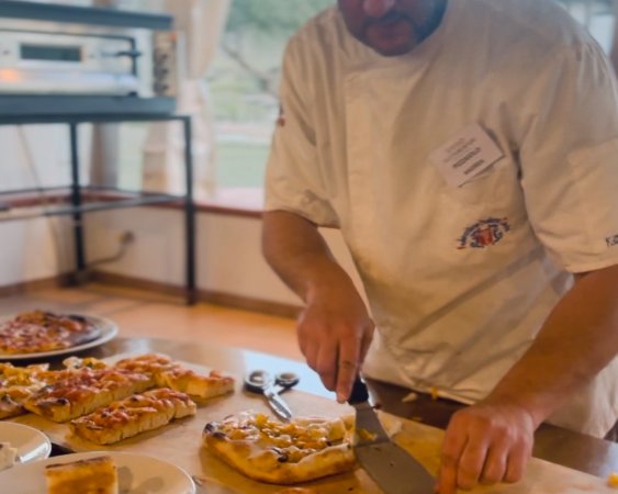 Un pizzaiolo taglia grandi fette di pizza su un tavolo di legno.