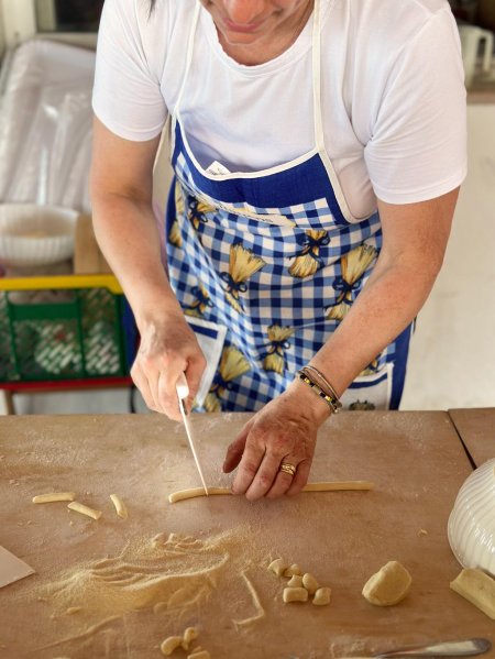 Una persona taglia la pasta su un tavolo con un coltello, indossando un grembiule blu a quadri.